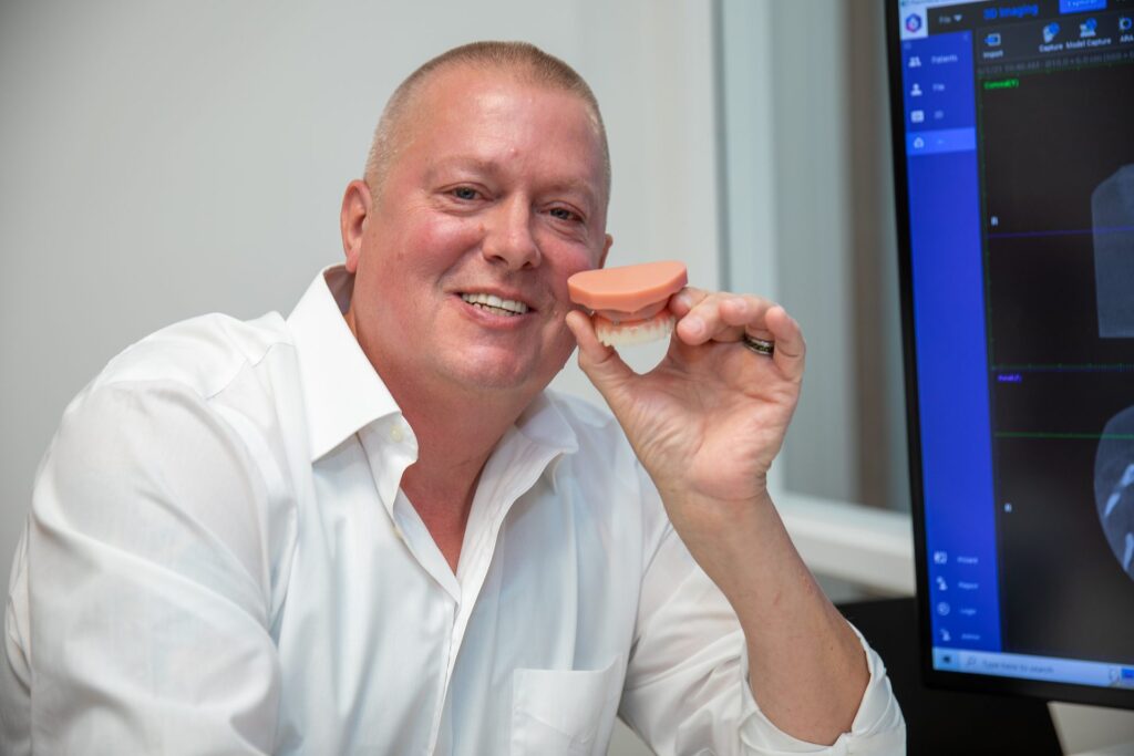 Smiling upper All-on-4 patient holding a full-arch model in the consultation room at Winchester Dental Implant & Sedation Center