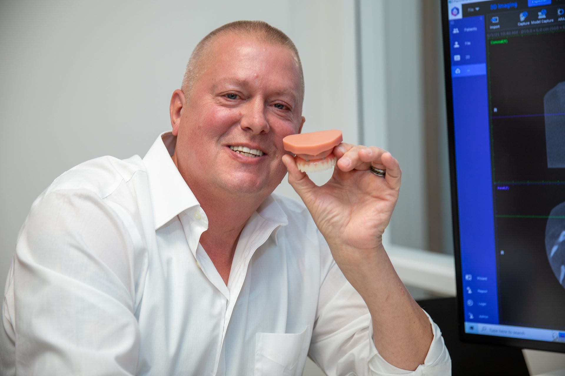 Smiling upper All-on-4 patient holding a full-arch model in the consultation room