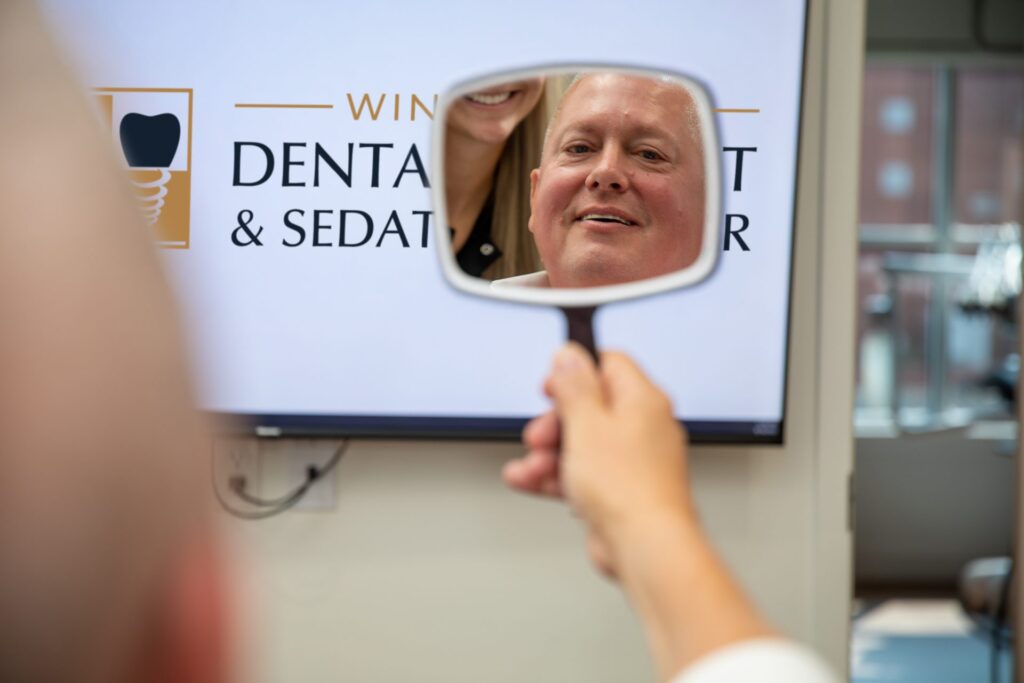 Upper All-on-4 patient admiring his new smile in a hand mirror