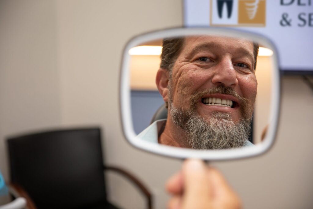Upper All-on-4 patient smiling at his new teeth in a hand mirror