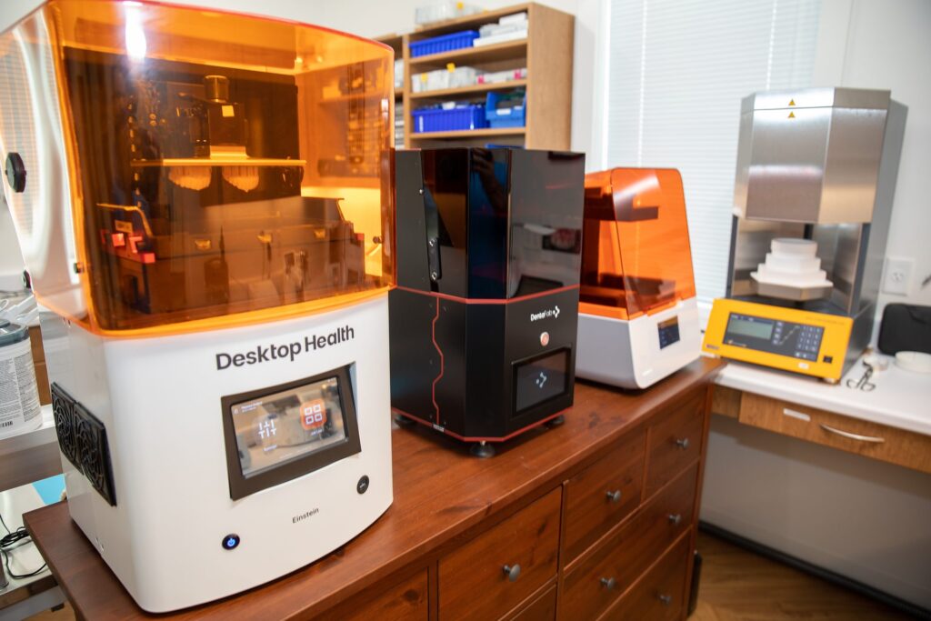Row of dental 3D printers, including Desktop Health and DentaFab units, in the in-house lab