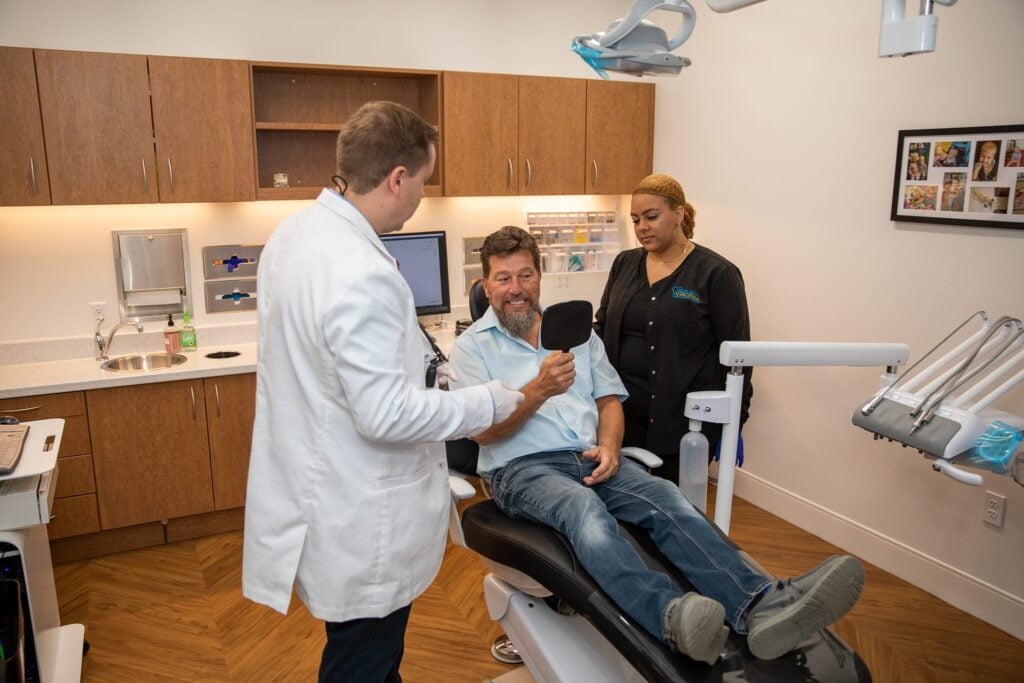 Dr. Niels Oestervemb with an upper All-on-4 patient checking his new smile in a hand mirror
