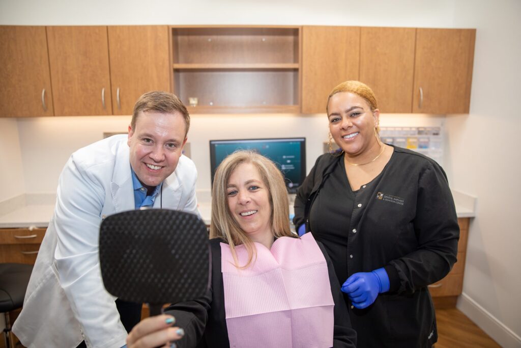 Full-mouth rehabilitation patient checking her new smile with Dr. Oestervemb and a dental assistant