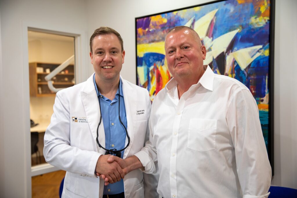 Dr. Niels Oestervemb and an upper All-on-4 patient shaking hands and smiling at the camera