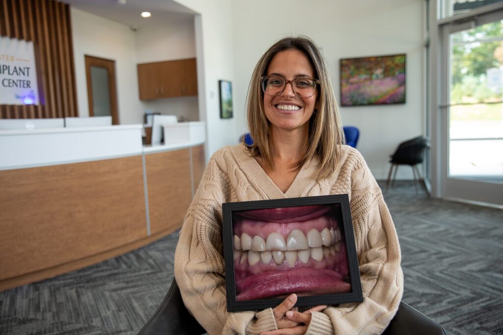 Full-mouth reconstruction patient smiling while holding a framed before photo of her teeth