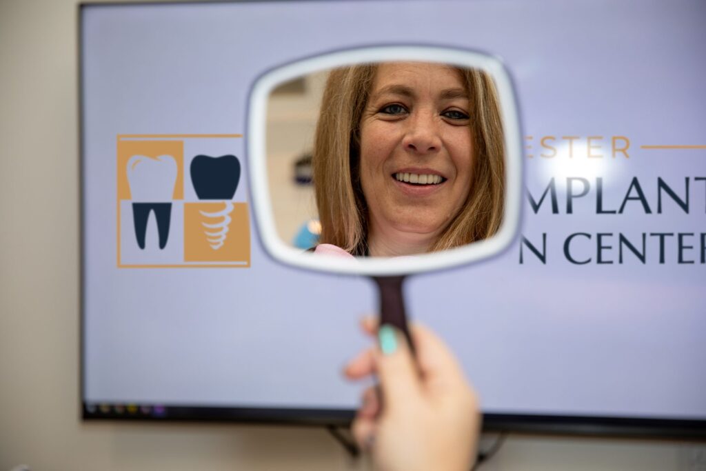 Full-mouth rehabilitation patient smiling at her new crowns in a hand mirror