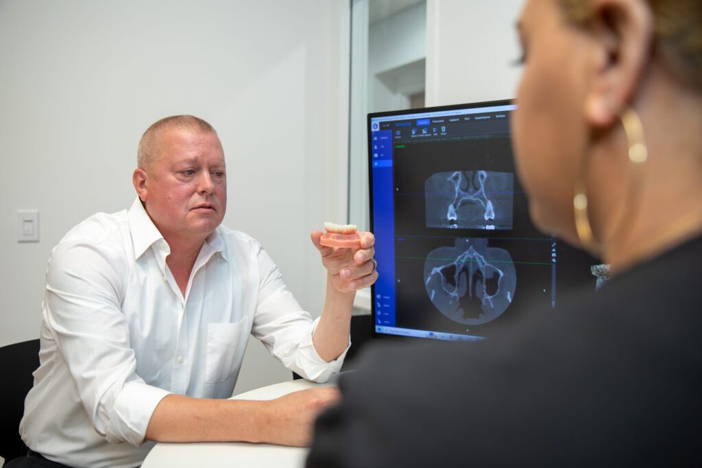 Dental implant patient holding an arch model while reviewing his 3D CT scan with a treatment coordinator