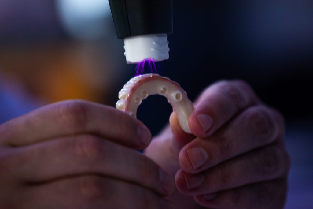 Technician curing a 3D-printed dental arch with a handheld UV light in the in-house lab